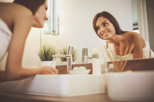 Young woman washing her face with clean water in bathroom