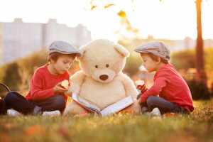 Two adorable little boys with his teddy bear friend in the park